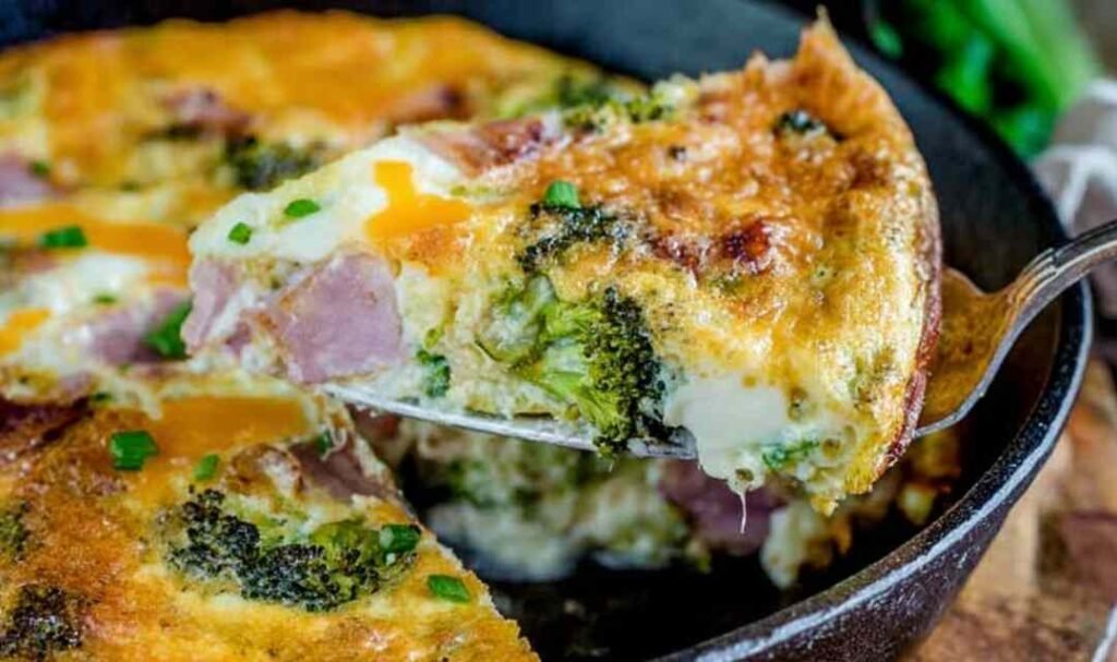 Cheesy ham and broccoli frittata in a cast iron skillet with golden brown top and visible cheddar cheese pockets