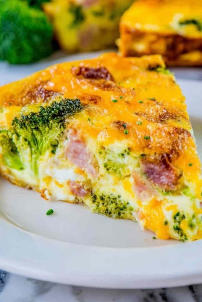Cheesy ham and broccoli frittata in a cast iron skillet with golden brown top and visible cheddar cheese pockets